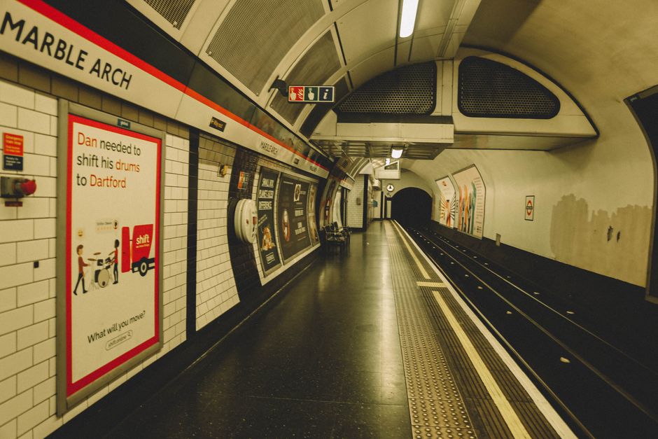 A clean and well-maintained underground subway station with tiled flooring in neutral tones, featuring a curved, white arched ceiling with modern lighting fixtures. The platform area is clear of debri